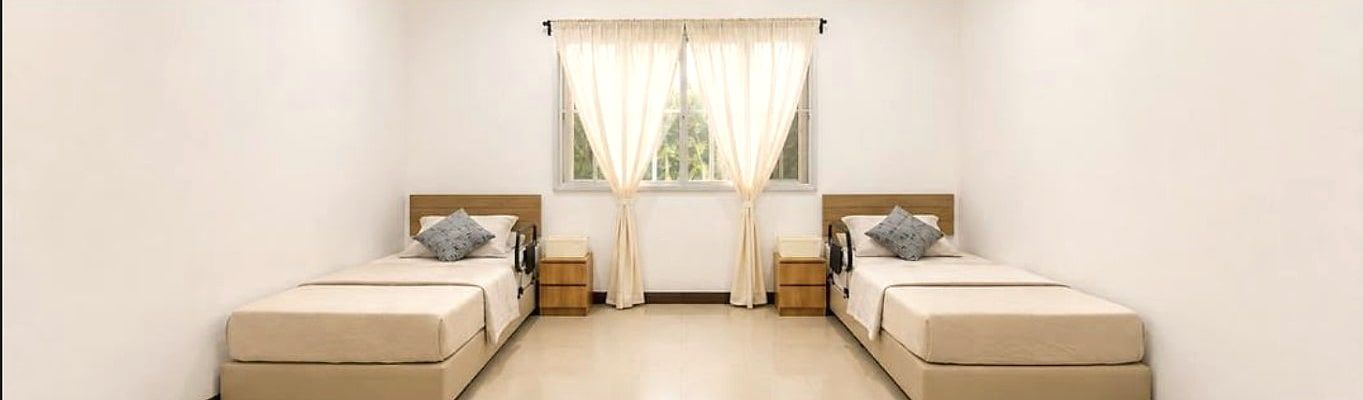 Renovated shared resident bedroom with two made-up beds and soft curtains